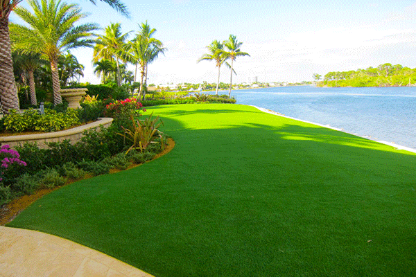 Luxury waterfront property featuring premium synthetic turf lawn, mature palm trees, private dock with boats, and sunset skyline views – professionally installed by JR Landscaping Service