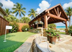 Backyard hardscape featuring a wooden pergola, custom putting green, stone patio, and tropical Florida plants with beach views in Madeira Beach, FL