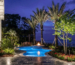 Luxury Clearwater Beach waterfront landscape architecture featuring a custom travertine pool deck, gas fire pit, and professional palm tree uplighting.